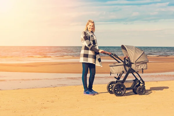 Lachende jonge moeder met kinderwagen op het strand — Stockfoto