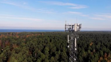 Orman ve mavi gökyüzü arka planında taşınabilir internet ağı için antenleri olan telekomünikasyon kulesine hava görüntüsü. 5G yayını