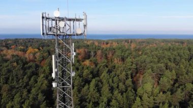 Orman ve mavi gökyüzü arka planında taşınabilir internet ağı için antenleri olan telekomünikasyon kulesine hava görüntüsü. 5G yayını