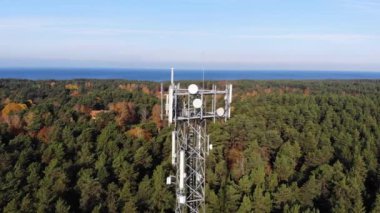 Orman ve mavi gökyüzü arka planında taşınabilir internet ağı için antenleri olan telekomünikasyon kulesine hava görüntüsü. 5G yayını