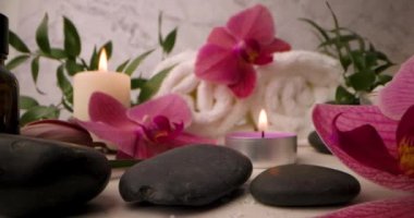 Spa malzemeleri - orkide çiçekleri, yanan mumlarla masaj taşları ve beyaz havlu ruloları. kaydırıcı atışı