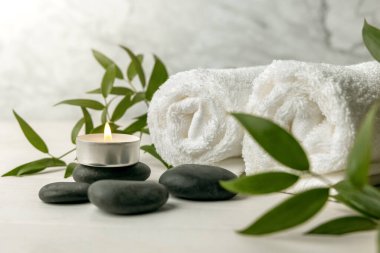 Beyaz havlulu spa taşları, yanan mum ve yeşil bitki