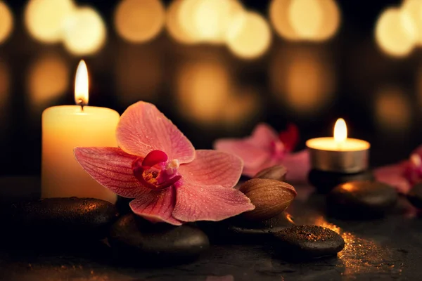 massage stones, orchid flower and burning candles on dark bokeh background at spa and wellness center