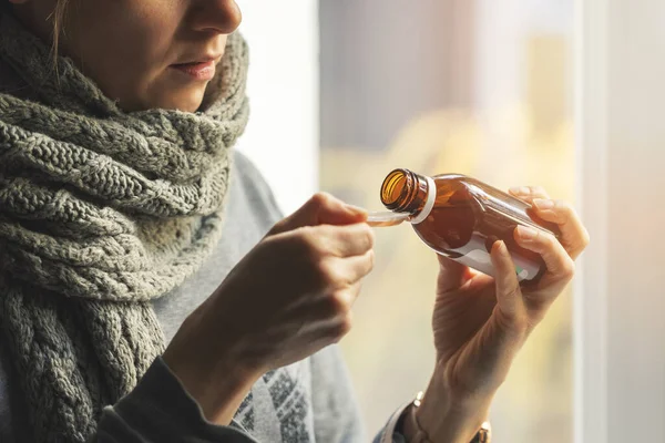 sick woman with scarf around the neck taking cough syrup at home