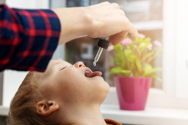 Anne çocuğuna damlatıcıyla vitamin damlası veriyor. Çocuklar için beslenme takviyeleri