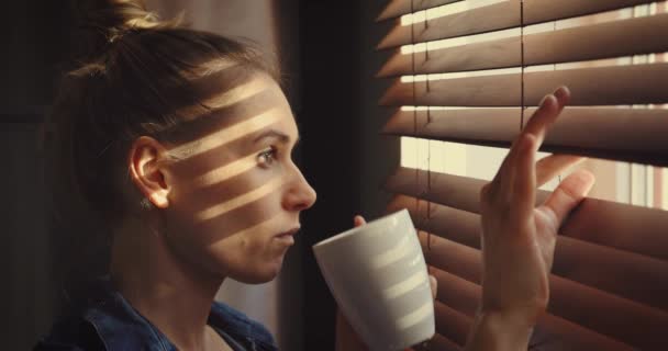 Kvinna Tittar Genom Fönstret Persienner Solljuset Och Dricka Kaffe — Stockvideo