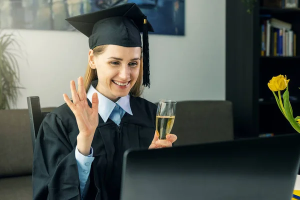 social distancing graduation party - female graduate wearing gown and celebrate bachelor degree online with college friends at home