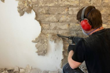Kapalı duvardaki alçıyı matkapla söken işçiler.