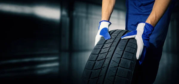 car tire shop and service - mechanic holding new tyre on garage background. copy space