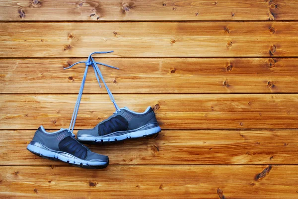 Pair of sport shoes hang on a nail on a brown wooden wall — Stock Photo, Image