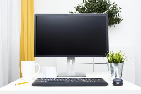 Monitor in bianco e accessori per ufficio sul tavolo in interni luminosi — Foto Stock