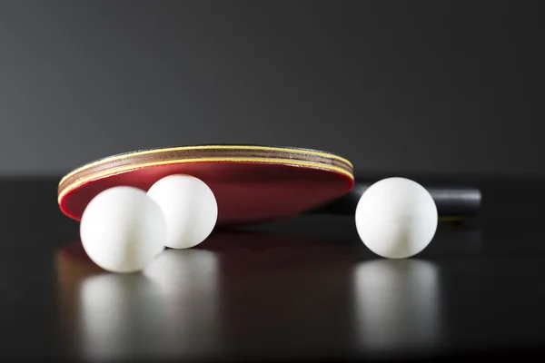 Raqueta de tenis de mesa y pelotas sobre mesa oscura — Foto de Stock