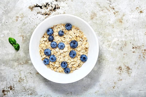 Raw oat flakes topped blueberries in white bowl