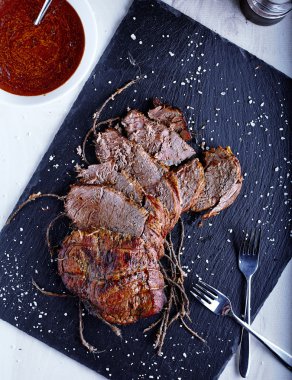 Roast beef on black stone board with sauce clipart