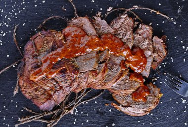Roast beef on black stone board with sauce clipart