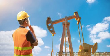 Petrol kulesi mühendisi ya da teknisyeni güvenlik kaskı ve ham petrol pompasıyla yansıtıcı yelek giyer.