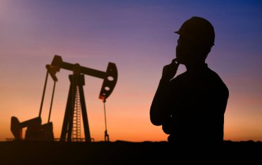 Petrol kulesi mühendisi ya da teknisyeni güvenlik kaskı ve ham petrol pompasıyla yansıtıcı yelek giyer.