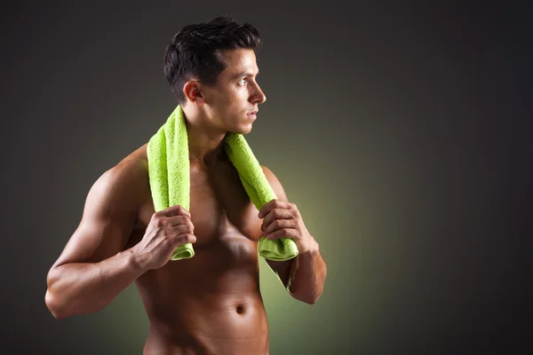 Homme sportif tenant une serviette verte sur fond noir — Photo