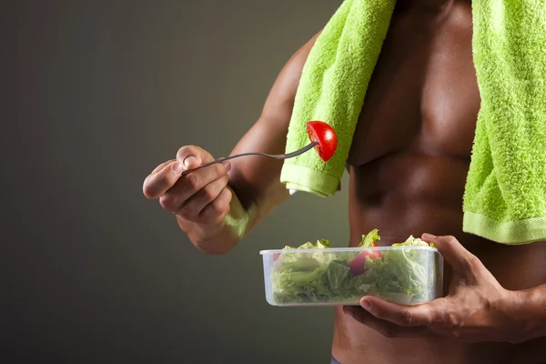 Uomo forte che tiene una ciotola di insalata fresca su sfondo nero — Foto Stock