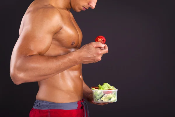 Hombre fuerte sosteniendo un tazón de ensalada fresca sobre fondo negro — Foto de Stock