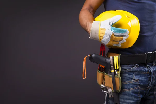 Close-up de um trabalhador com cinto de ferramentas e capacete contra costas pretas — Fotografia de Stock