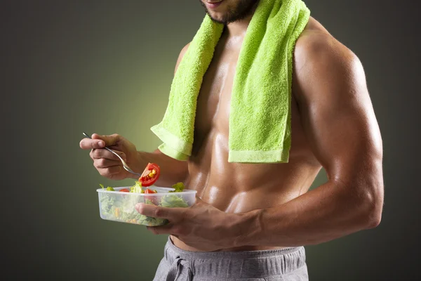 Homem de fitness segurando uma tigela de salada fresca no fundo preto — Fotografia de Stock