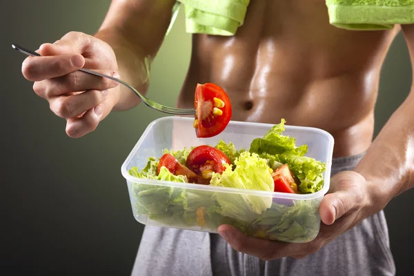 Fitness man holding a bowl of fresh salad on black background — Stock Photo, Image