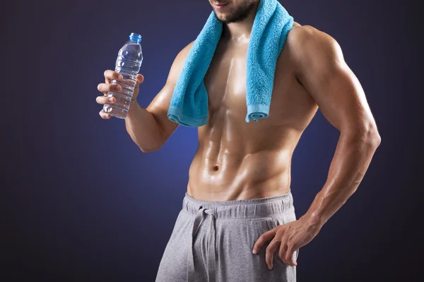 Homem de fitness segurando uma garrafa de água doce no fundo preto — Fotografia de Stock