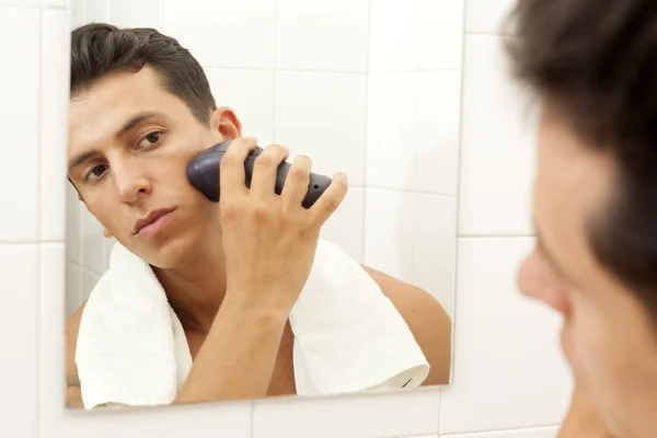 Joven afeitándose con afeitadora eléctrica en el baño — Foto de Stock