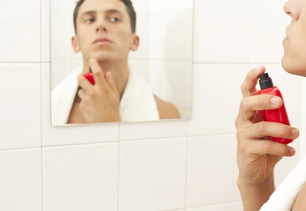 Красивий молодий чоловік наносить парфуми у ванній кімнаті — стокове фото