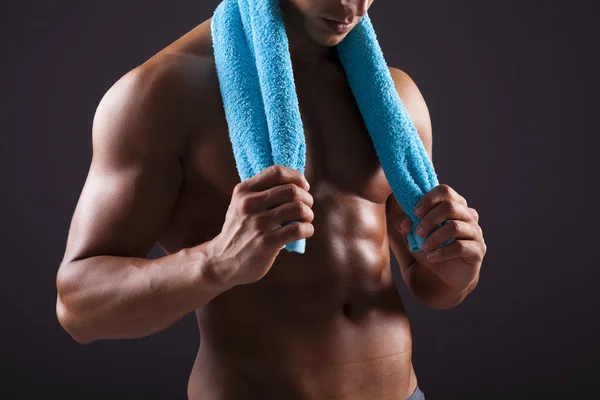 Homem atlético segurando uma toalha azul no fundo preto — Fotografia de Stock
