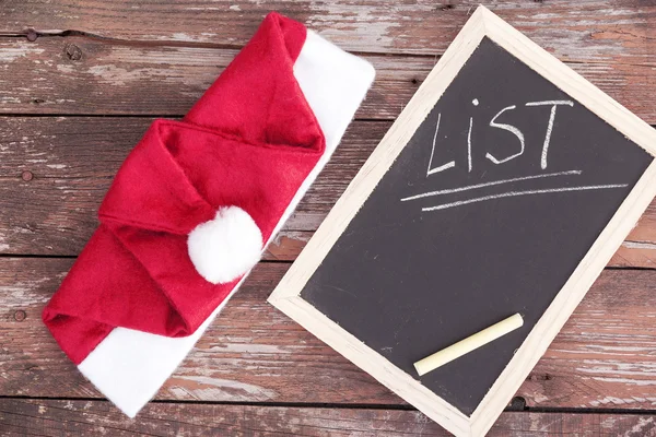 Santa claus hat and chalkboard on a wooden background — Stock Photo, Image