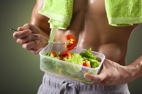 Close-up of a fitness man holding a bowl of fresh salad on black