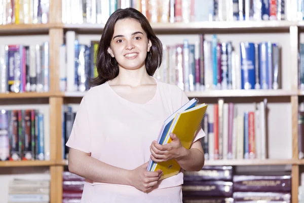 Estudante feminina segurando livros na biblioteca — Fotografia de Stock