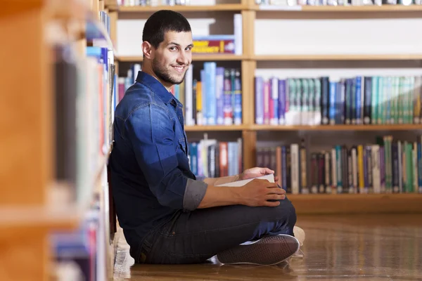 Estudante do sexo masculino lendo um livro na biblioteca — Fotografia de Stock