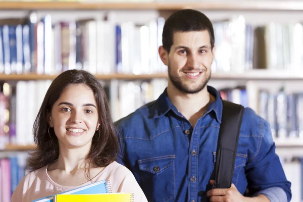 Estudantes sorrindo em pé na biblioteca — Fotografia de Stock