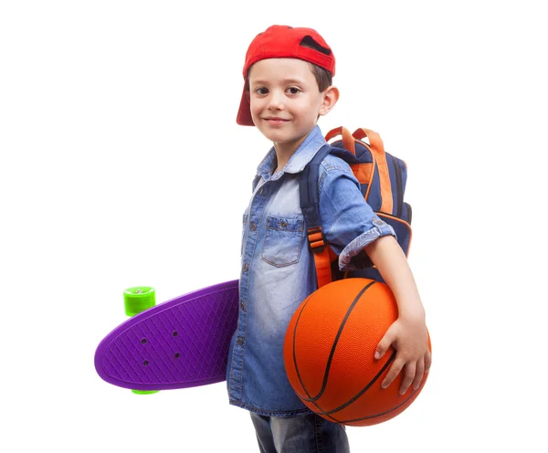 Niño de la escuela sosteniendo un monopatín y un baloncesto — Foto de Stock