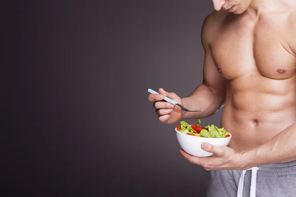 Atletisk man håller en skål med färsk sallad — Stockfoto