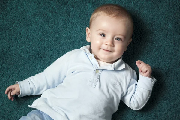 Bebê adorável deitado em um tapete azul — Fotografia de Stock