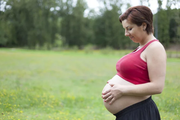 Kobieta w ciąży trzymając jej brzuch na zewnątrz — Zdjęcie stockowe