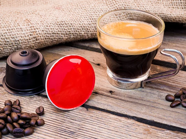 Cup of coffee and pods on wooden table