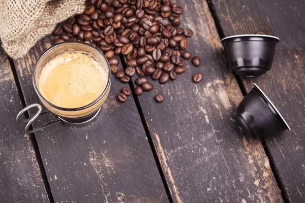 Šálek kávy a kapsle na dřevěný stůl — Stock fotografie