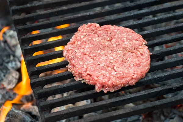 Raw hamburger slice cooking on grill with flames — Stock Photo, Image