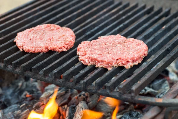 Alevler ile ızgarada pişirme iki ham hamburger dilimleri