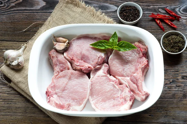 Rauw varkensvlees Loin Steaks in een schotel op houten tafel — Stockfoto