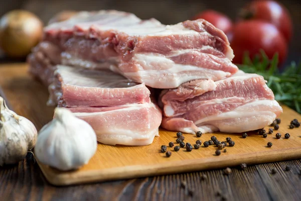 Feche a carne crua de porco na placa de madeira com um frasco de especiarias — Fotografia de Stock