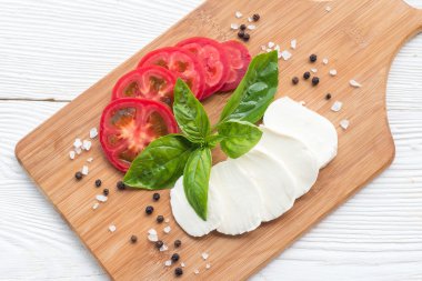 Mozzarella peyniri, domates ve taze fesleğen yaprakları kesme tahtası üzerinde