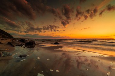 Deniz kenarında gün batımı. Taşlar, kum ve deniz batan güneşin ışınlarıyla aydınlandı..