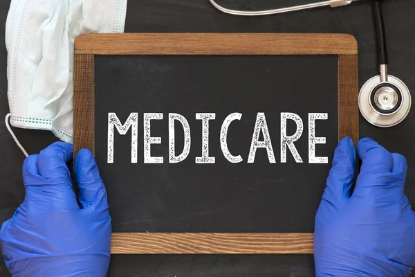 Doctor holding blackboard with the word medicare — Stock Photo, Image