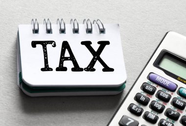 Ofis defterinde, gri bir arkaplanda hesap makinesinin yanında bir vergi kelimesi. Vergi İş Konsepti .